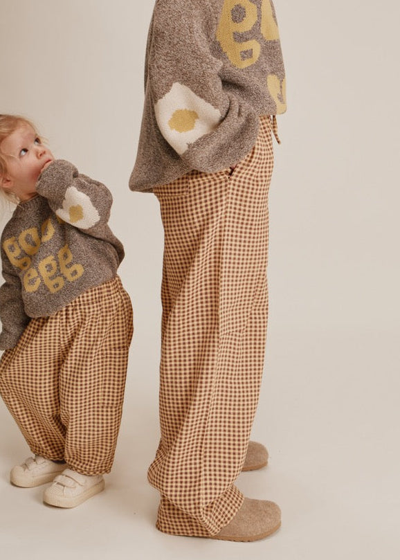 Two people wearing matching brown and beige outfits with patterned pants on a plain background