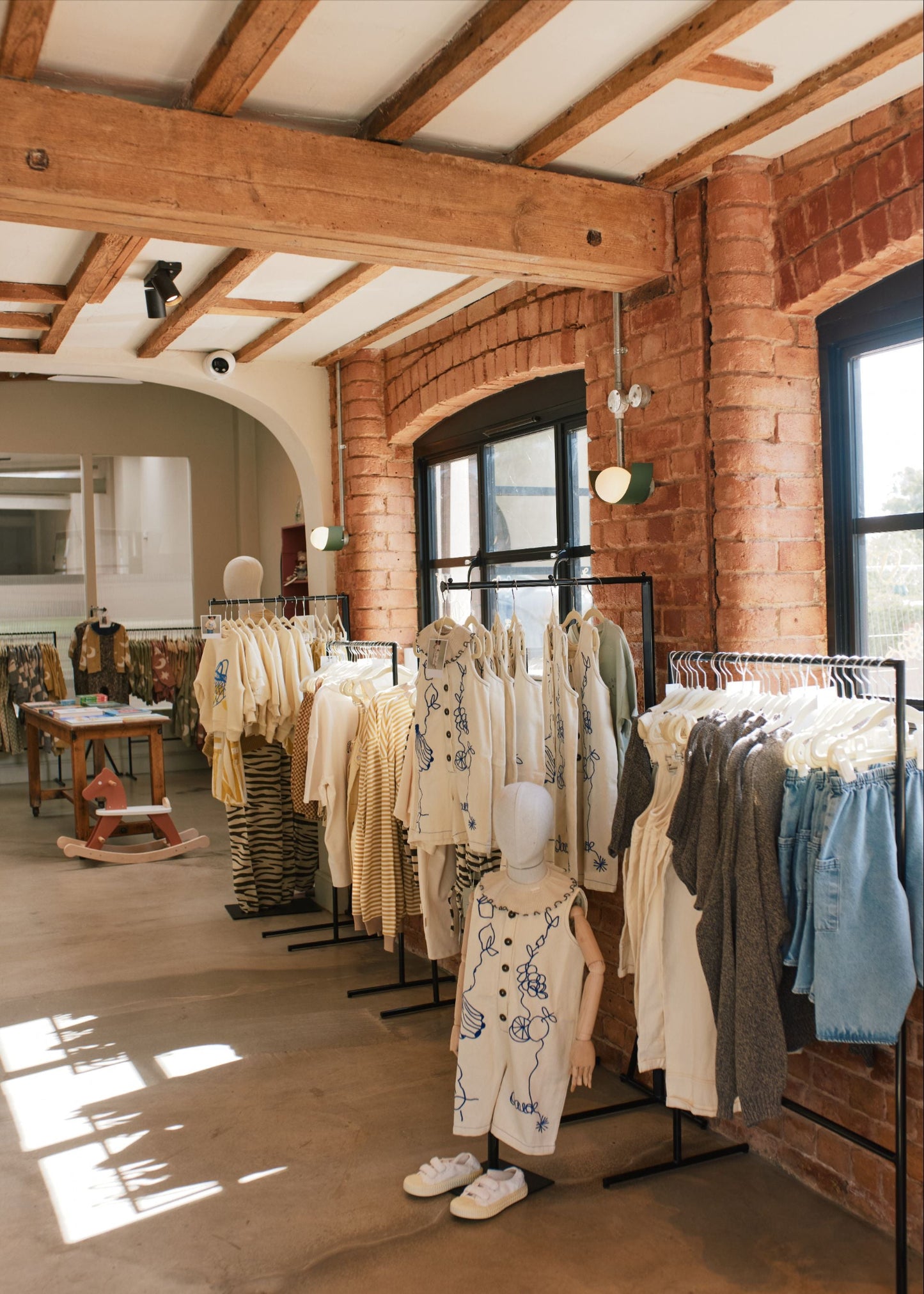 Fashion store interior with racks of clothing and mannequins against a brick wall.
